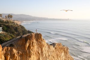 A person standing on a cliff overlooking the ocean.